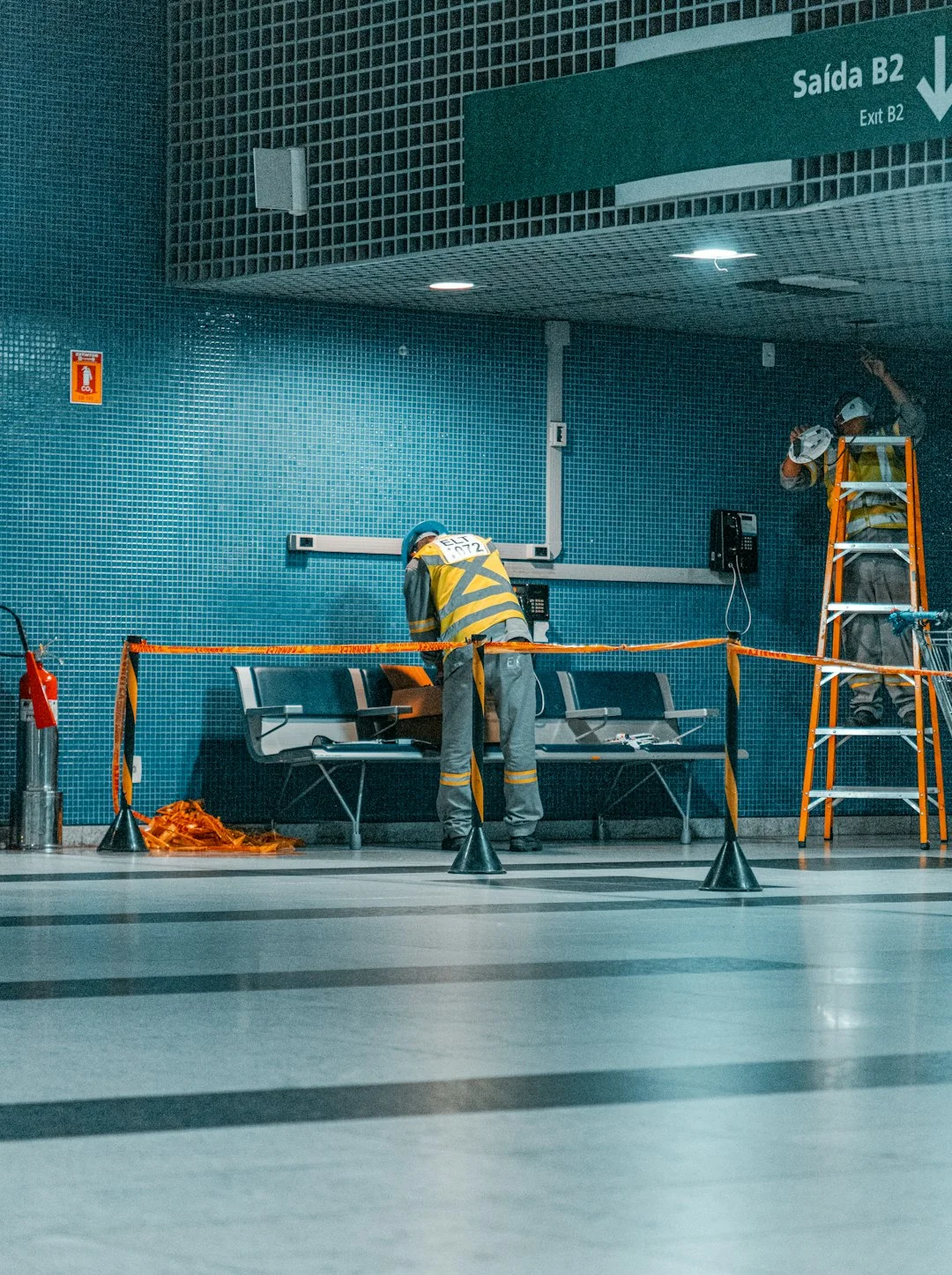 A brightly lit industrial hallway with a cleaning cart and supplies near an office door.